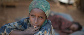 Una niña sentada a la sombra, mientras su hermana duerme, en un campamento de desplazados en Baidoa, Somalia. Foto de la ONU / Tobin Jones